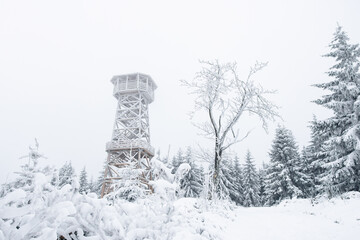 A snow-covered wooden lookout tower on top of the Czernica Mountain. Winter landscape in the Sudetes on a hiking trail.