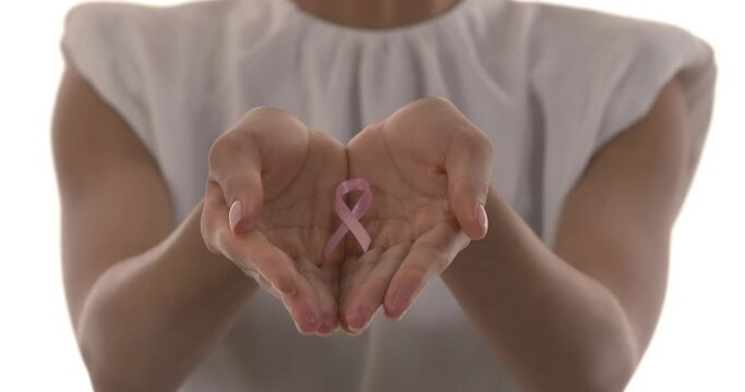 Blurred cropped image of young woman in t-shirt with pink ribbon in palms. World breast cancer day concept. Pink October. Focus on ribbon. Isolated on white background