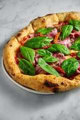 Delicious pizza with roast beef, sun-dried tomatoes, pickled onions, cheese and spinach on a white plate on a white marble background