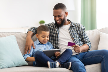 African Father And Son Shopping Online Using Digital Tablet Indoor