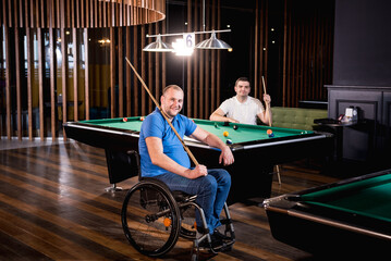 Adult men with disabilities in a wheelchair play billiards in the club