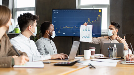 Employee in protective medical mask showing paper with graph diagram