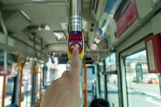 日本のバスの降車ボタンを押す指と「止まります」の表示が点灯している場面