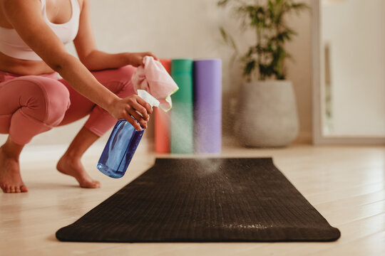 Woman cleaning exercise mat with disinfectant spray in gym