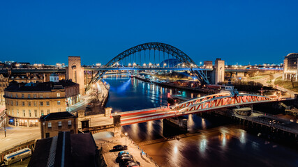 Newcastle upon Tyne UK: 30th March 2021: Newcastle Gateshead Quayside at night, with of Tyne Bridge and city skyline, long exposure during blue hour - obrazy, fototapety, plakaty