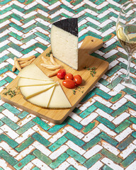 Spanish Manchego cheese sliced with some cherry tomatoes and a glass of white wine over a green and white table.