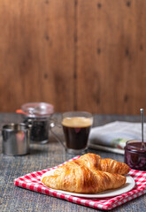 Breakfast with croissants, marmalade and coffee with a newspaper on the background.