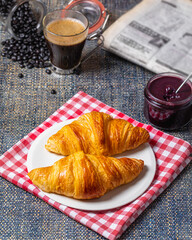 Breakfast with croissants, marmalade and coffee with a newspaper on the background.