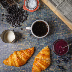 Breakfast with croissants, marmalade and coffee with a newspaper on the background.