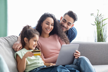 Fototapeta premium Booking Vacation Online. Happy family using laptop and credit card at home