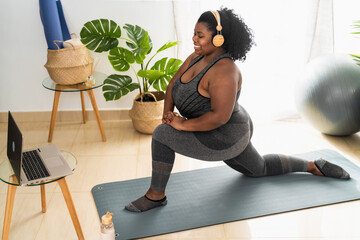 Young  African curvy woman doing pilates fitness class with laptop at home - Sport wellness people...