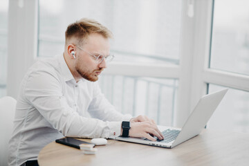 Fototapeta na wymiar young man in glasses wearing wireless headphones works with laptop, video conference