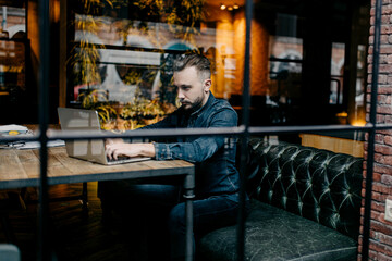 Male freelancer sits in a cozy coworking cafe and works online with a laptop, online business	