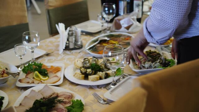 The waiter serves a festive table and puts plates of food on the table. Close-up shooting