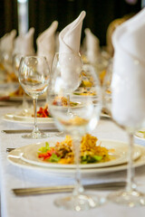 Close-up of a banquet set table: wine / champagne glasses, napkins and salad. For a solemn holiday