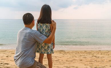 Asian father and little daughter together on the beach, view at the back of father and daughter looking to apparent horizon from the beach, beautiful sea wave and sky in a morning, space for copy.
