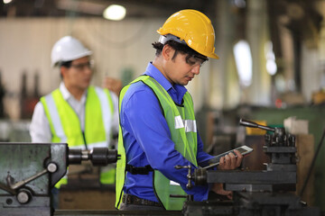 Asian mechanic worker in safety hard hat and reflective cloth is working with lathe machine inside the factory for industry business concept