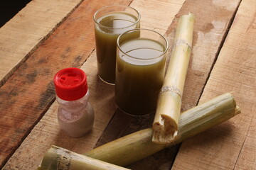 Sugarcane juice in glass with piece of sugarcane and black salt on wooden table 