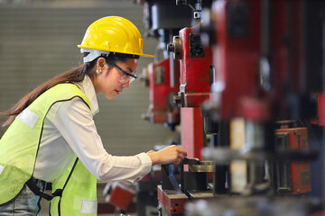 Asian female mechanic worker in safety hard hat and reflective cloth is working with lathe machine...