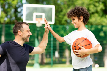 Portrait of man and boy giving high five playing basketball - Powered by Adobe