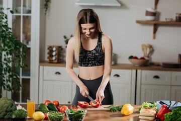 Fit young woman cooking fresh salad at home standing in kitchen adding exotic spices to mixture. Healthy eating concept.