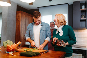 Older parents with their son prepare a healthy breakfast. Son is chopping vegetables for salad.