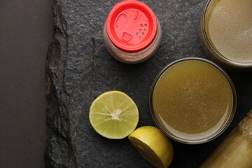 Obraz na płótnie Canvas Sugarcane juice in glass with piece of sugarcane, lemon and black salt 
