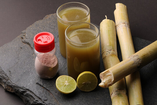 Sugarcane juice in glass with piece of sugarcane, lemon and black salt 