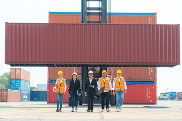Portrait Of man woman Engineers and asian Factory workers walking in front of machine lift container and cargo space. Business people with confident and smart working in shipping transport industry.