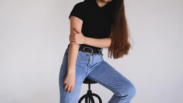 Girl are sitting on a spinning bar stool. Black T-shirt and blue jeans. The young woman moves and touches her long hair.