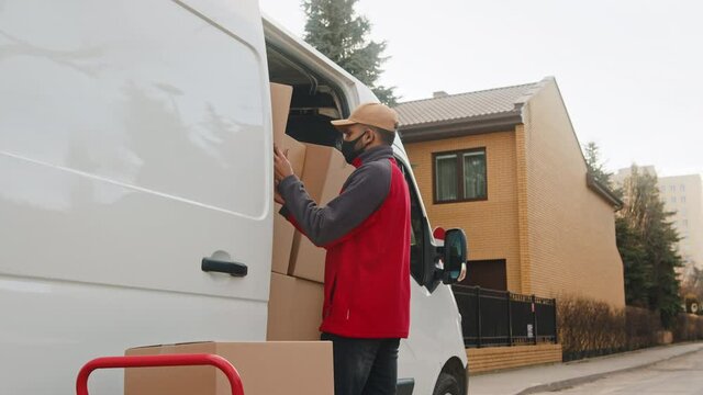 Young man with face mask loading van with cardboard boxes. High quality 4k footage