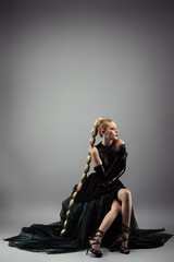 Pretty young blonde woman in evening dress, wearing a long braid, sitting, in profile