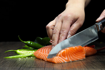 Salmon is in the hands of the Japanese chef and meticulously done, He is using a knife to slice salmon fillet for sashimi and sushi