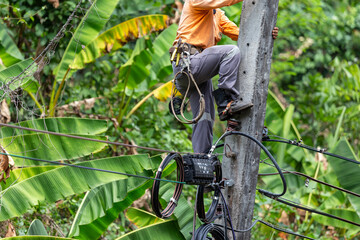 Electrician workers with tools for cutting and connecting wires Climb the electric pole, tilt it, repair the broken wires. It's a very risky job. The electric pole tilts, causing a summer storm.