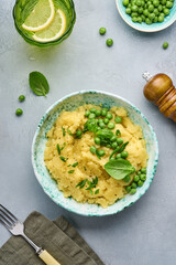 Mashed potato with butter, green peas, onions, basil in a white bowl on a light slate, stone or concrete background. Top view with close up.