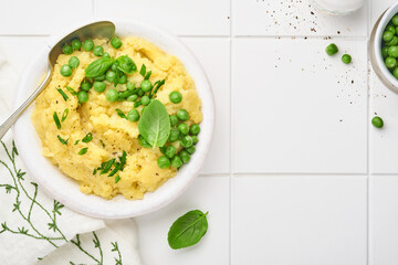 Mashed potato with butter, green peas, onions, basil on white ceramic tile background. Top view with close up.