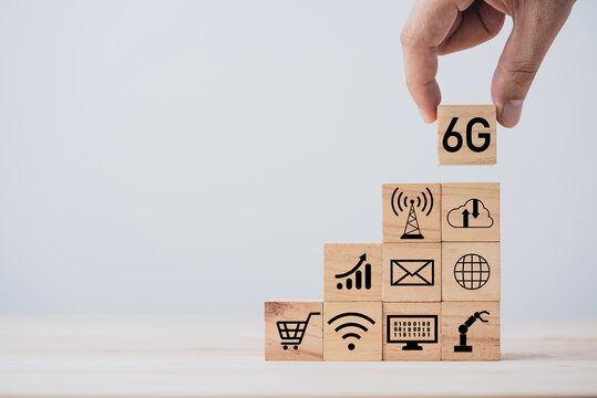 Hand putting 6G which print screen on wooden cube block and technology icon , six generation of high speed internet technology which will change communication and lifestyle in the future.