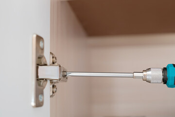 Adjustment of fittings, door hinge, cabinet door with a screwdriver. Home renovation concept, furniture assembly. Close-up, copyspace.