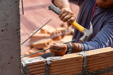 Close-up Construction workers are hammering rebar to cement columns to stabilize the masonry to increase the stability of the brick wall.