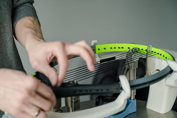 Close-up of tennis racket on electronic stringing machine. Process of replacement synthetic gut string before game. Hands of stringer out of focus.