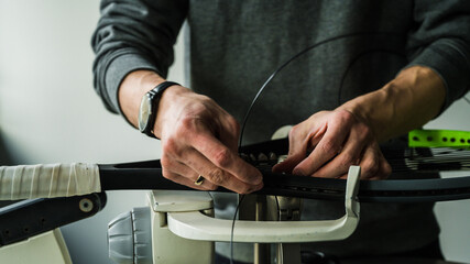 Close-up of tennis racket on electronic stringing machine. Process of replacement synthetic gut string before game. Hands of stringer.