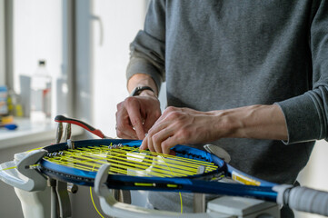 Close-up of tennis racket on electronic stringing machine. Process of replacement synthetic gut string before game. Hands of stringer.