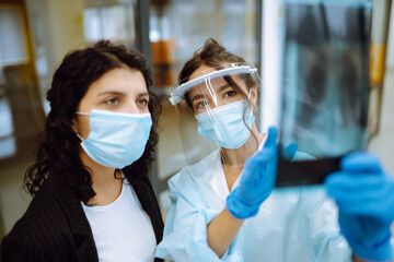Young  doctor in visor and protective gloves and patient discussing an x-ray. Pneumonia.X-rays of light. Fluorography. Covid-2019
