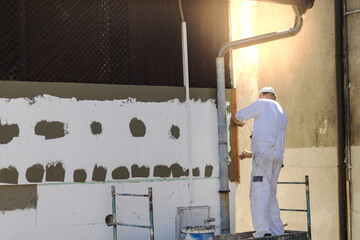 Adult male renovating a factory and puttying the walls under the lights