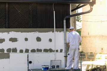 Adult male renovating a factory and puttying the walls under the lights