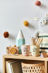 Stylish scandinavian newborn baby room with toys, plush animal, photo camera and child accessories. Cozy decoration and hanging cotton balls on the white wall. Close up.