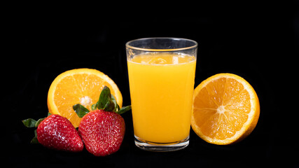 Glass of freshly squeezed orange juice, halved orange and strawberries, on black background