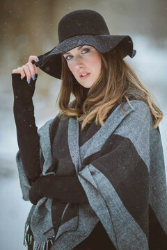 Portrait Of A Young Woman Wearing A Hat And Oversized Blanket Scarf Standing Outside In Winter