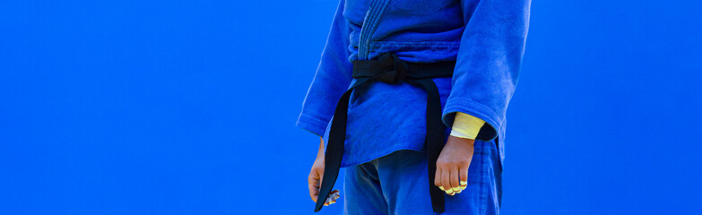 Judo fighter poses in blue kimono with black belt. Japanese judo and jiu jitsu