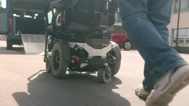 Close up of assistant helping disabled person on wheelchair with transport using accessible vehicle ramp